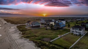 Una zona residencial costera con casas sobre pilotes, una playa de arena y un atardecer sobre el océano.