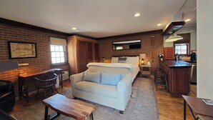 A hotel room with a bed, a desk, a chair, a sofa, and a kitchen area.