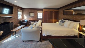 A bedroom with a brick wall, a fireplace, a bed, a desk, a chair, and a TV.