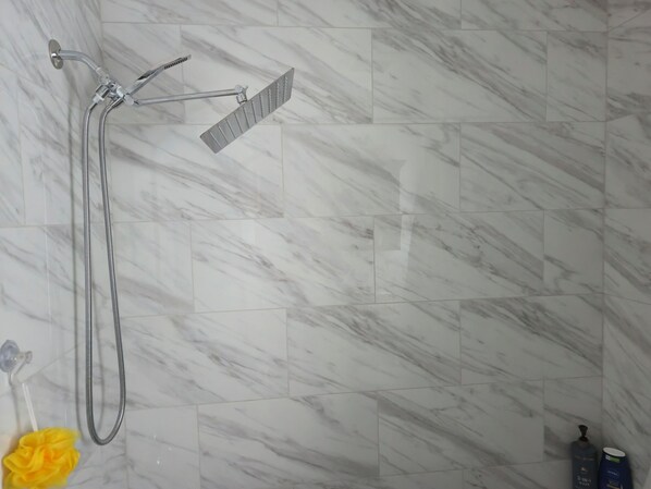 A bathroom with a shower, marble tiles, a yellow bath sponge, and two bottles of shampoo.