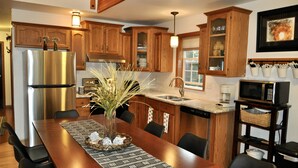 A modern kitchen with wooden cabinets, stainless steel appliances, and a dining area with a long table and chairs. - Take me to the Trees! Lakefront on Autumn Lake, 3min to Salmon River (Orwell)