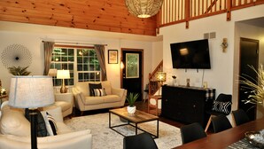 A living room with a sofa, coffee table, and TV. There is a staircase and a dining area with chairs. - Take me to the Trees! Lakefront on Autumn Lake, 3min to Salmon River (Orwell)
