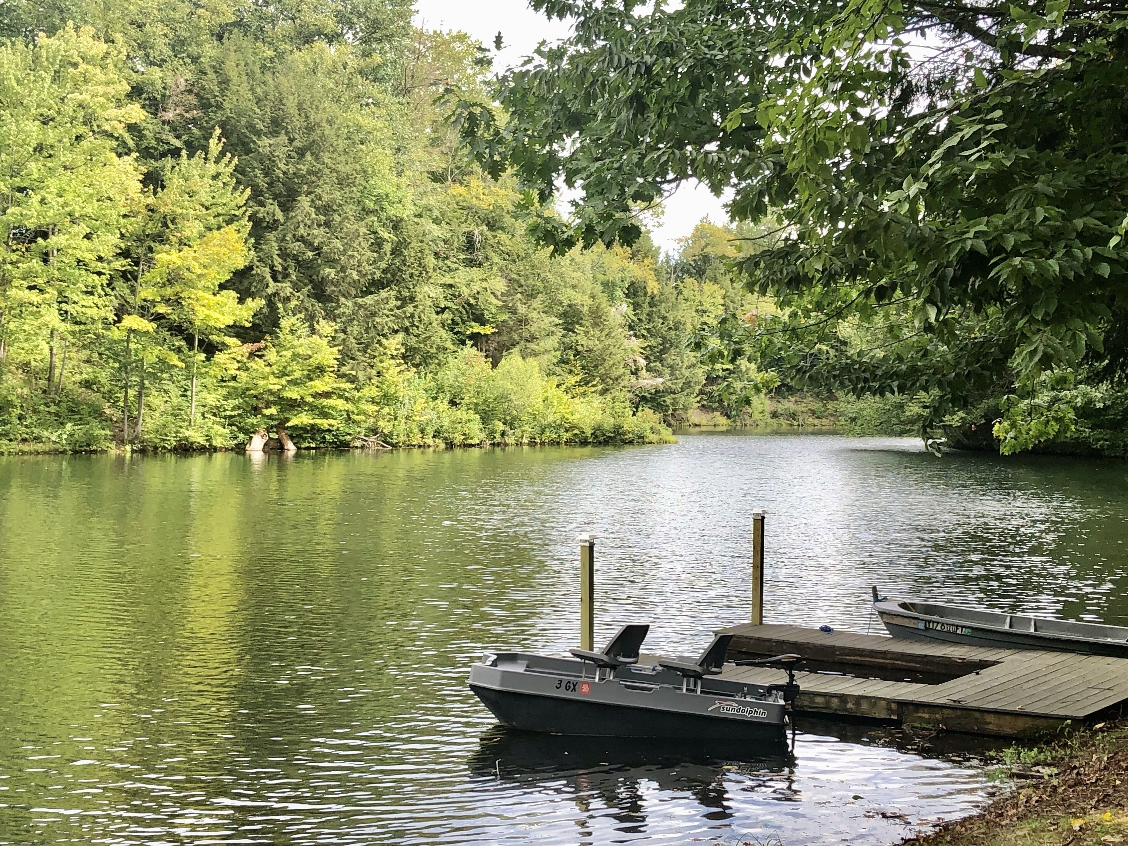 A calm river with a dock and a boat named 'sundolphin' anchored at the dock.