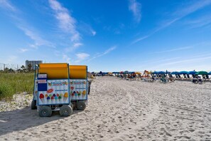 A beach with a food cart selling Italian ice.