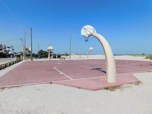 An outdoor basketball court with two hoops, a bench, and a clear sky.