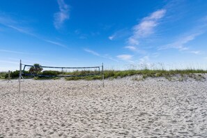 A beach volleyball net on a sandy beach with sparse vegetation.