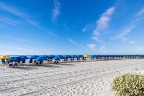 Uma praia com fileiras de guarda-sóis e espreguiçadeiras azuis e amarelas.