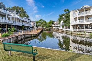 A canal with buildings on either side, a bench in the foreground, and a clear sky.