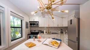 Una cocina moderna con armarios blancos, una isla central, un refrigerador de acero inoxidable y una lámpara colgante original.