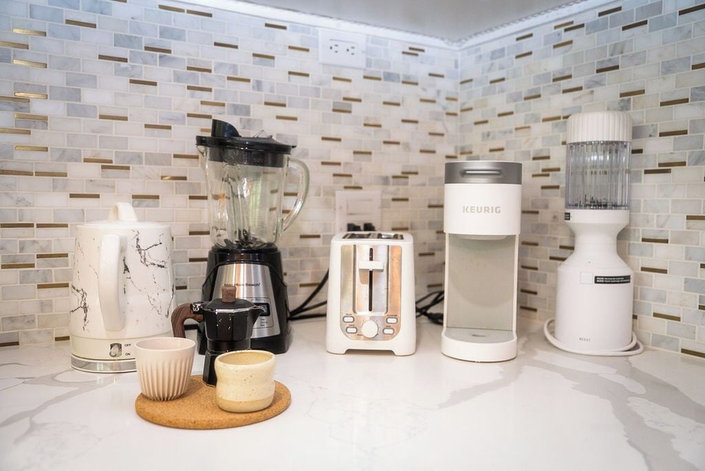 A kitchen with a coffee maker, toaster, blender, and a kettle on a countertop.