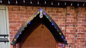 A wooden bench with a slatted seat and backrest, supported by a black frame with a pointed roof. - Garden cottage self catering  (Collingham)