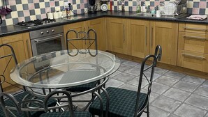 A kitchen with a round glass table, checkered chairs, wooden cabinets, and a tiled backsplash. - Garden cottage self catering  (Collingham)