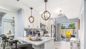 Une cuisine moderne avec des meubles blancs, un îlot central doté de tabourets et des luminaires suspendus.