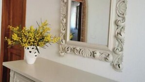 A white dresser with ornate carvings and black knobs, a white vase with yellow flowers, and a large ornate mirror on the wall. - Villa Verde Cefalù sea view 2 (Cefalù)
