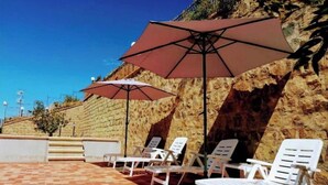 A patio area with white lounge chairs and large umbrellas, a stone wall, and a clear blue sky. - Villa Verde Cefalù sea view 2 (Cefalù)