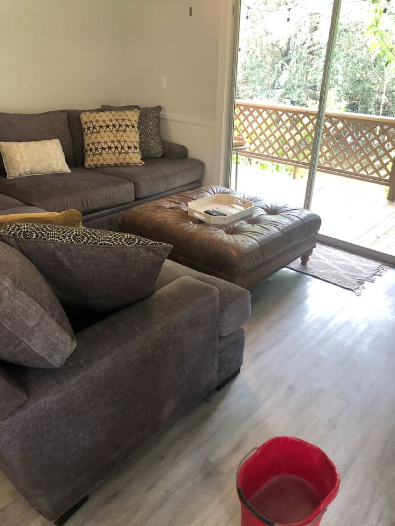 A living room with a grey sofa, patterned cushions, and a red bucket on the floor.