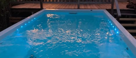 An outdoor swimming pool with a wooden deck and string lights.