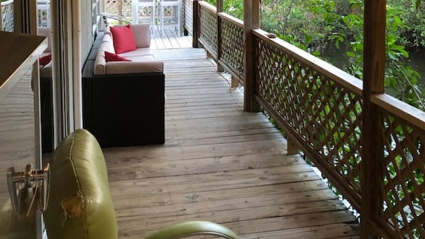 Une terrasse extérieure couverte, dotée d’un ventilateur de plafond, de rampes en bois et d’un espace salon avec des coussins.
