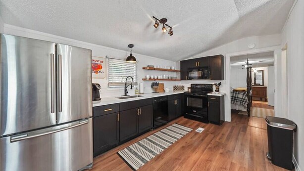 A compact kitchen with a stainless steel refrigerator, black cabinets, a microwave, and a stove. - Lake Conroe 3BR | Boat Ramp, Fire Pit, Fenced Yard, Sleeps 8, Pet-Friendly (Willis)