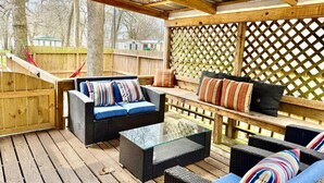 An outdoor patio with wicker furniture, a glass coffee table, and a wooden deck. - Lake Conroe 3BR | Boat Ramp, Fire Pit, Fenced Yard, Sleeps 8, Pet-Friendly (Willis)