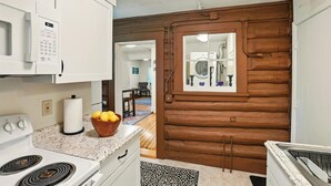 A kitchen with white cabinets, a microwave, a stove, and a wooden door leading to a laundry area. - Coastal Cabin - Downtown Historical Log Home (Anchorage)