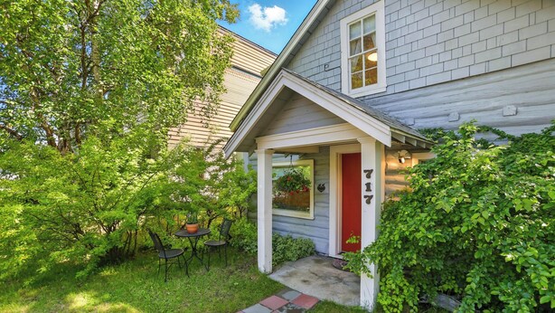 A house with a porch, a red door, and a small garden area with chairs and tables. - Coastal Cabin - Downtown Historical Log Home (Anchorage)