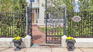 A gated entrance with a wrought iron gate, a brick pathway, and two planters with yellow flowers. - Historic, Recently Renovated Home Near Savannah River & Downtown Augusta! (Augusta)