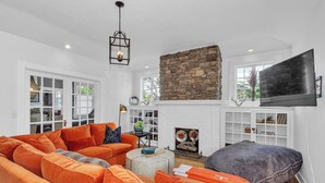 A living room with a large orange sectional sofa, a round coffee table, a stone fireplace, and a flat-screen TV mounted on the wall. - Historic, Recently Renovated Home Near Savannah River & Downtown Augusta! (Augusta)