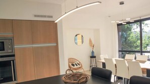 Una cocina moderna con armarios de madera, horno integrado y comedor con mesa negra y sillas blancas.