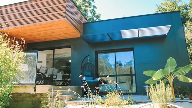 Una casa moderna con techo de madera inclinado, ventanas grandes y una silla colgante en la zona de estar al aire libre.
