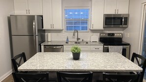 Una cocina moderna con armarios blancos, electrodomésticos de acero inoxidable, encimera de granito y una mesa de comedor con cuatro sillas.