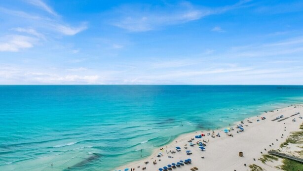 A beach with clear turquoise water, a sandy shore, and a pier extending into the sea.
