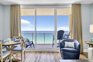 A room with a balcony, a dining table with chairs, a sofa, and a view of the ocean.