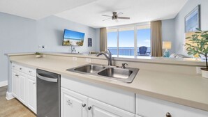 A modern kitchen with a large window, a ceiling fan, and a view of the ocean.