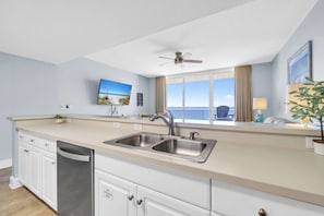 A modern kitchen with a large window, a ceiling fan, and a view of the ocean.
