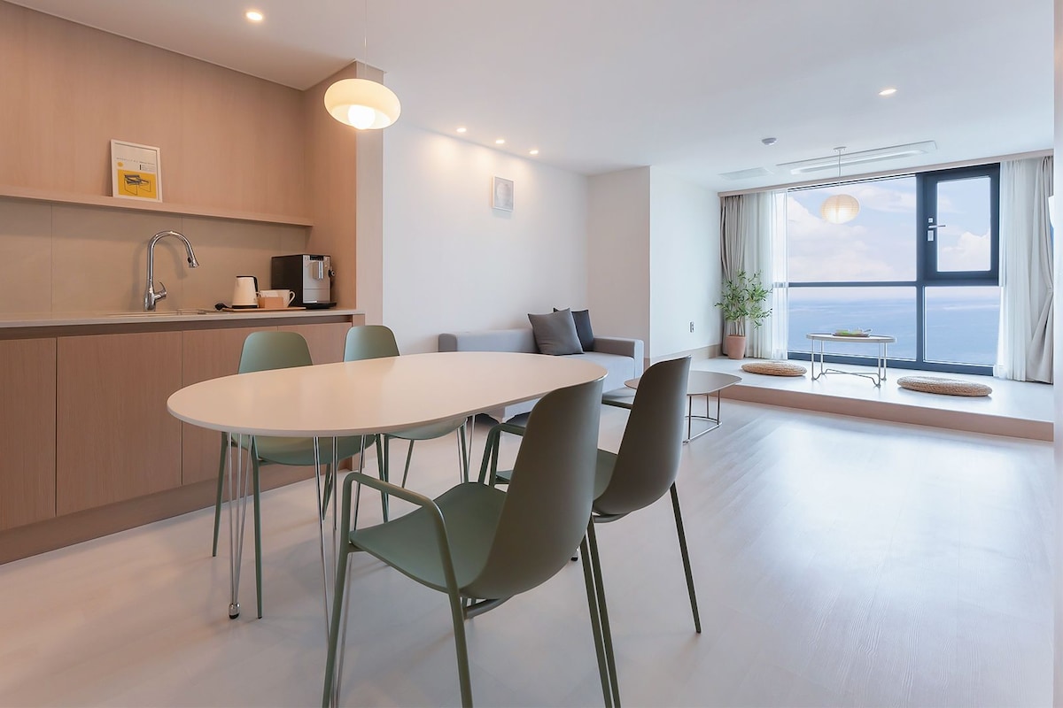 A modern kitchen with a dining area, a large window with a view, and a minimalist design.