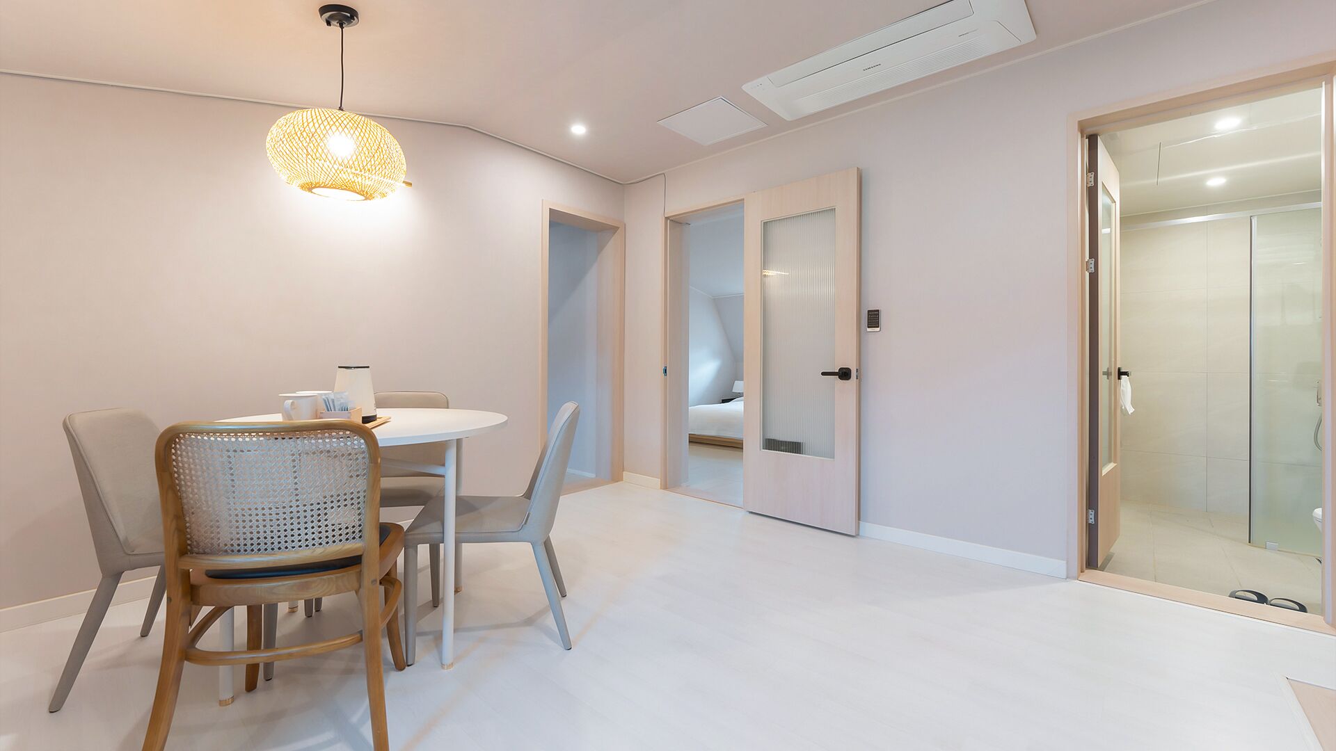 Una habitación moderna y bien iluminada con comedor, cabina de ducha de vidrio y una puerta que conduce a otra habitación.