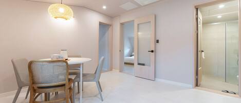 Una habitación moderna y bien iluminada con comedor, cabina de ducha de vidrio y una puerta que conduce a otra habitación.