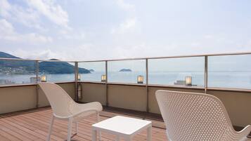 A deck with two white chairs and a small table, overlooking a calm sea with distant islands.