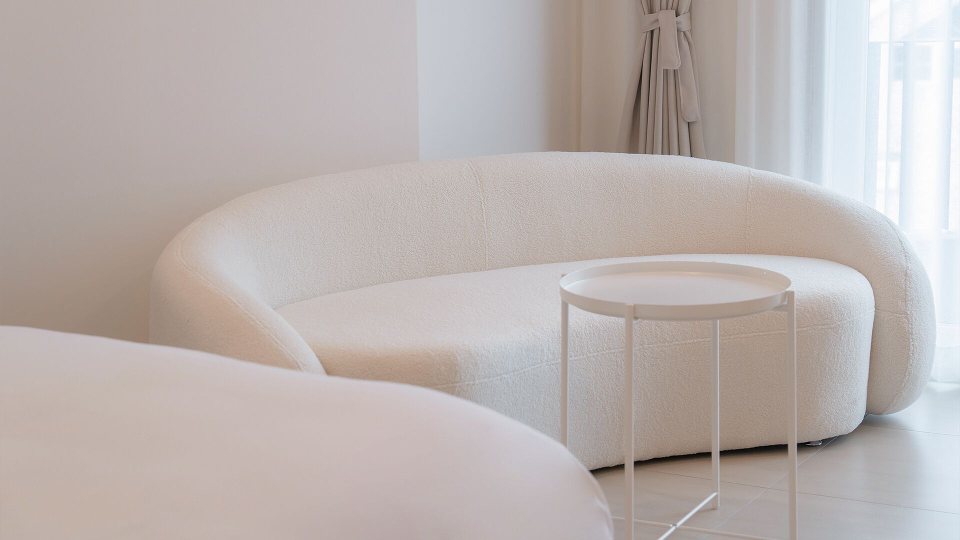 Een moderne, minimalistisch ingerichte kamer met een grote, gebogen witte bank en een klein witte bijzettafeltje.