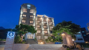 A multi-story hotel with a prominent entrance, a well-lit facade, and a sign indicating the name and address. - H.Avenue (Geoje)