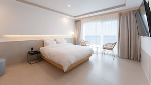 A modern hotel room with a large bed, bedside table, chair, and a view of the sea. - H.Avenue (Geoje)