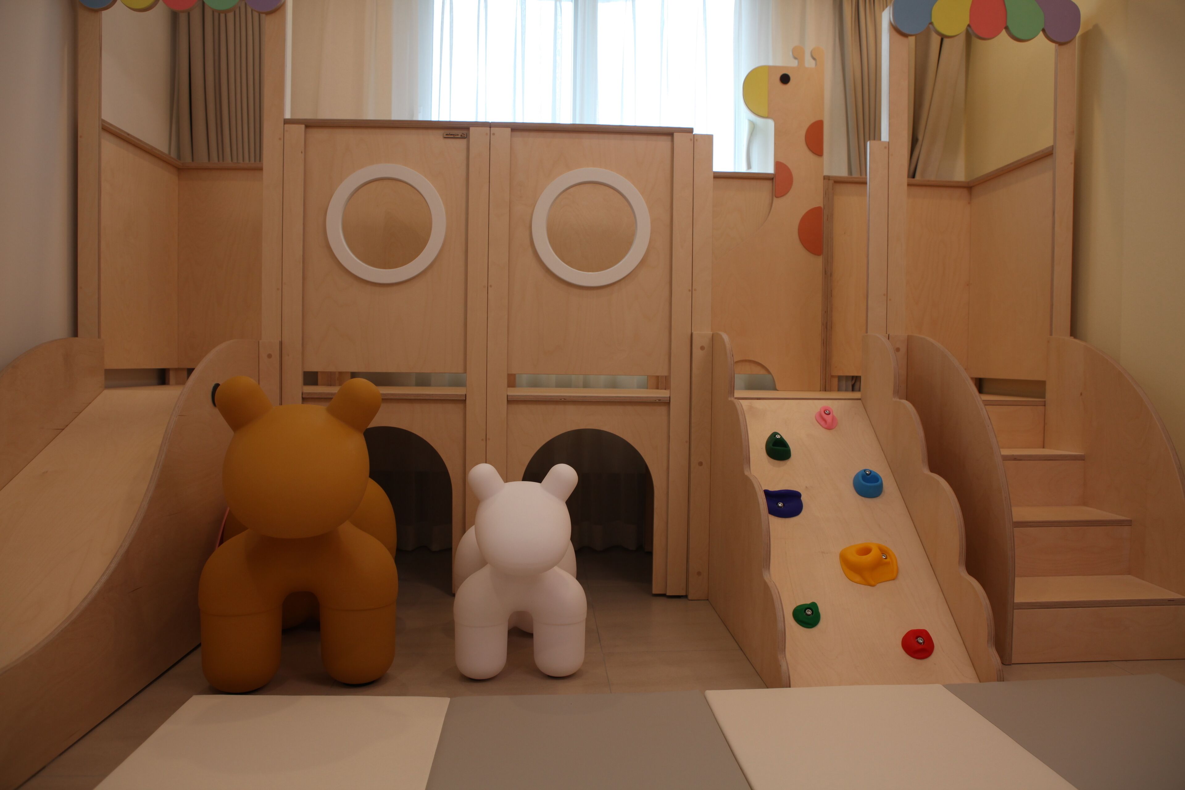 Ein Kinderspielbereich mit Rutsche, Kletterwand und zwei spielzeugartig gestalteten Bärenfiguren.