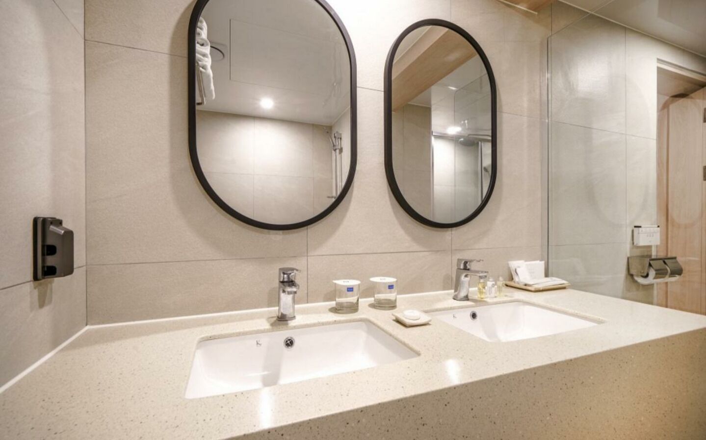 A modern bathroom with two sinks, a mirror, and a towel dispenser.