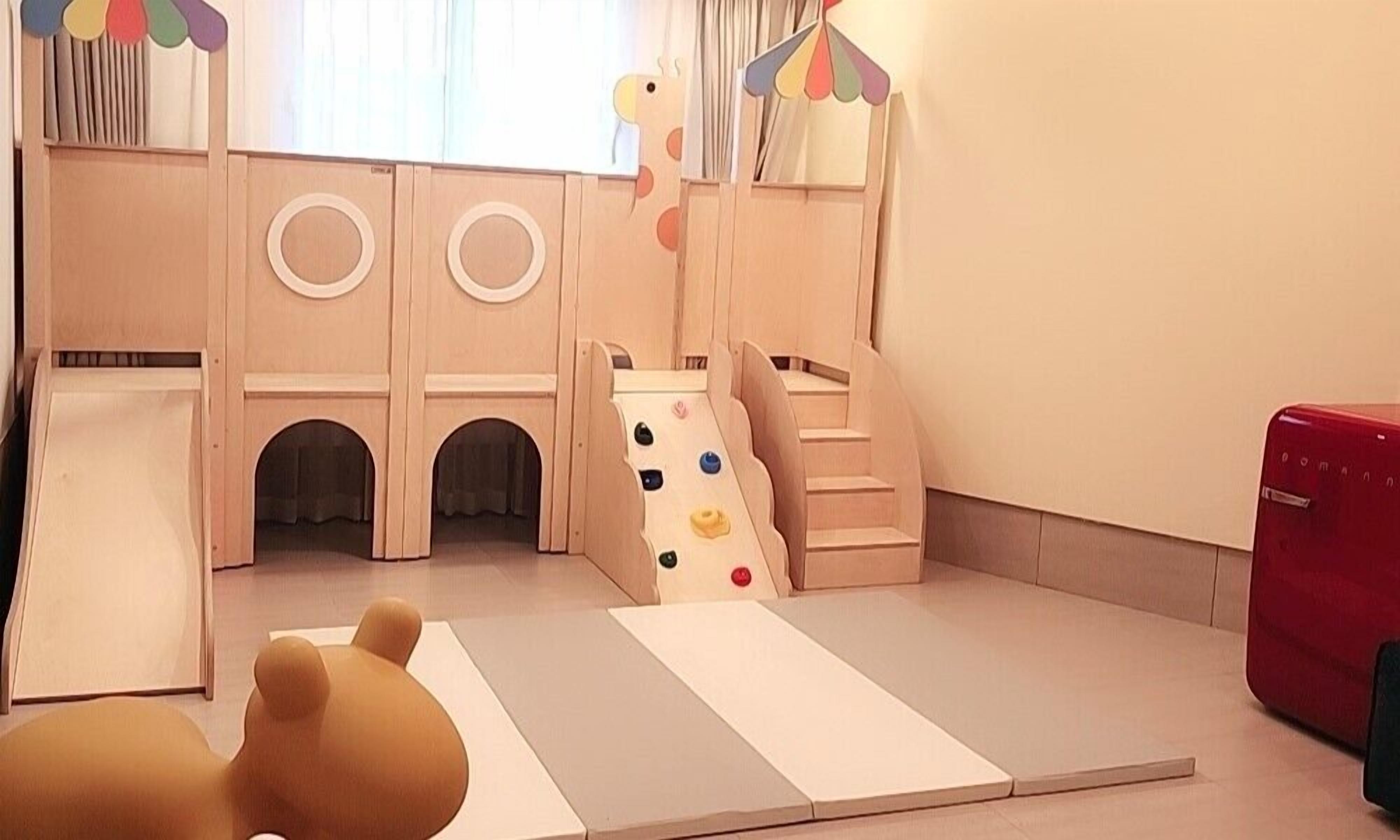 Zona de juegos infantiles con tobogán, escaleras de acceso y colchonetas acolchadas.