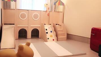 Zona de juegos infantiles con tobogán, escaleras de acceso y colchonetas acolchadas.