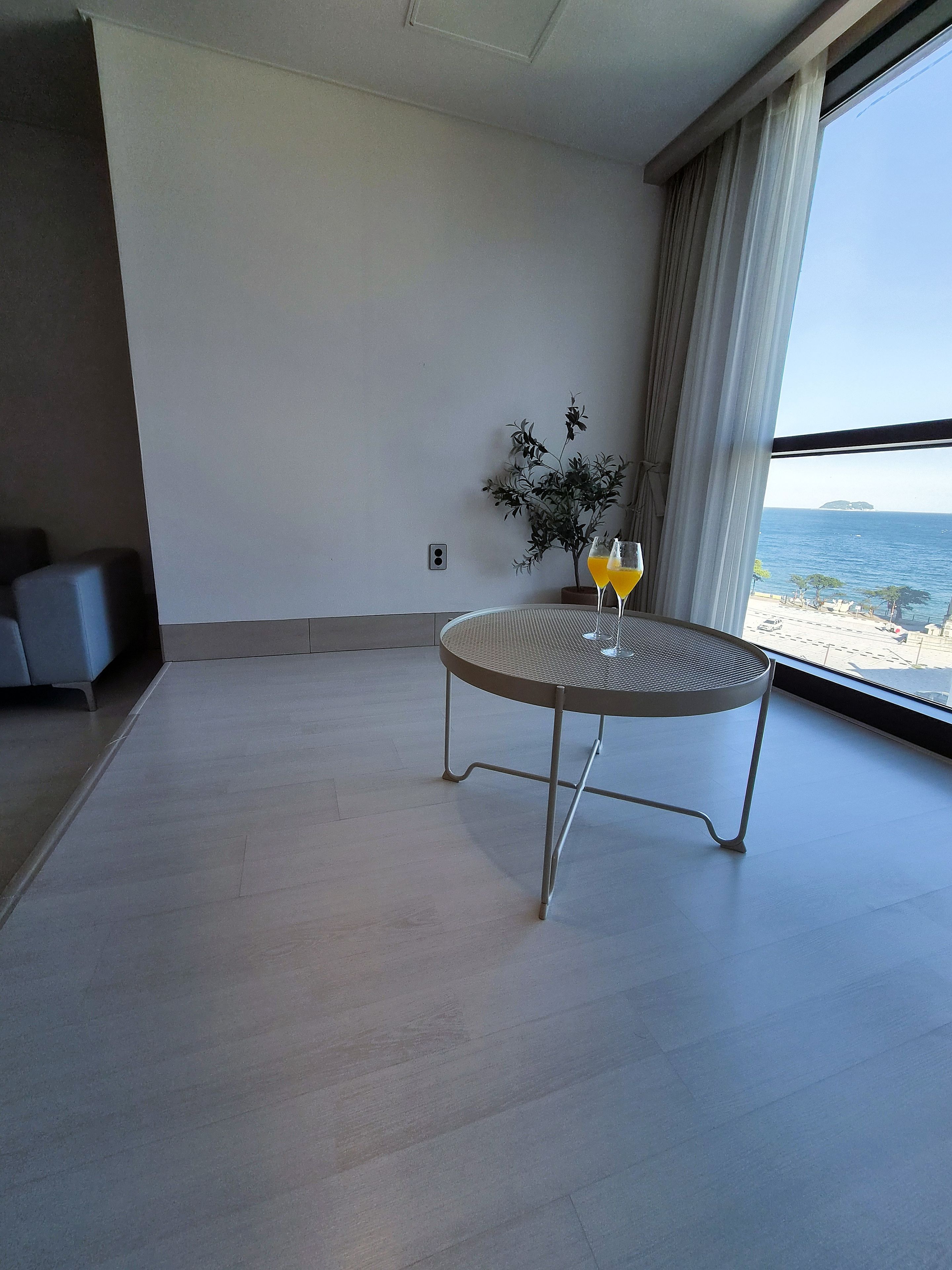 Una habitación moderna con una mesa redonda, dos vasos de jugo de naranja, una planta en maceta y vistas al mar.