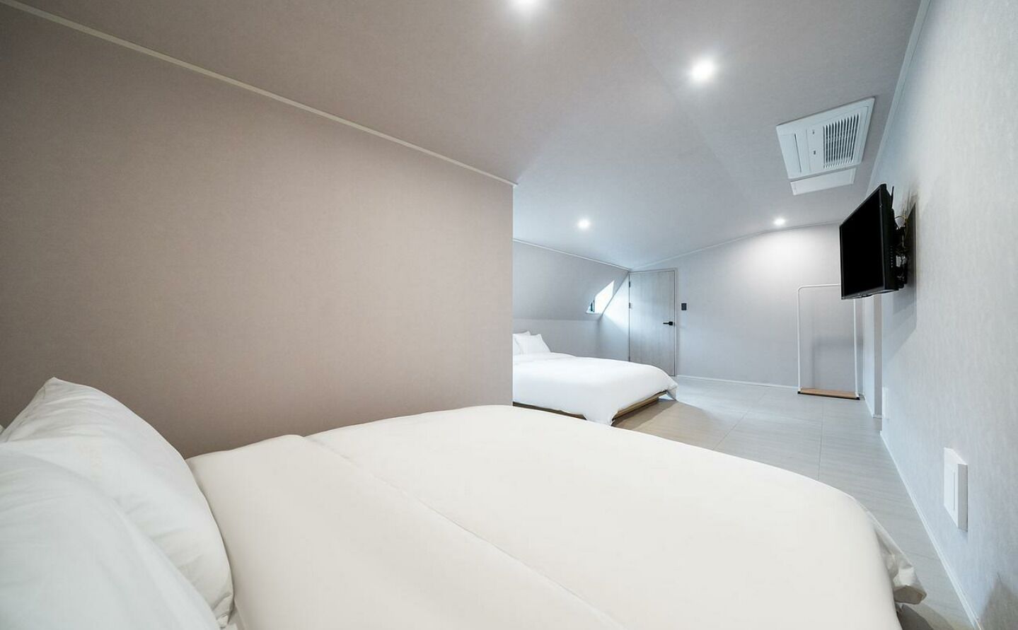 A modern bedroom with a large bed, a smaller bed, and a TV mounted on the wall.
