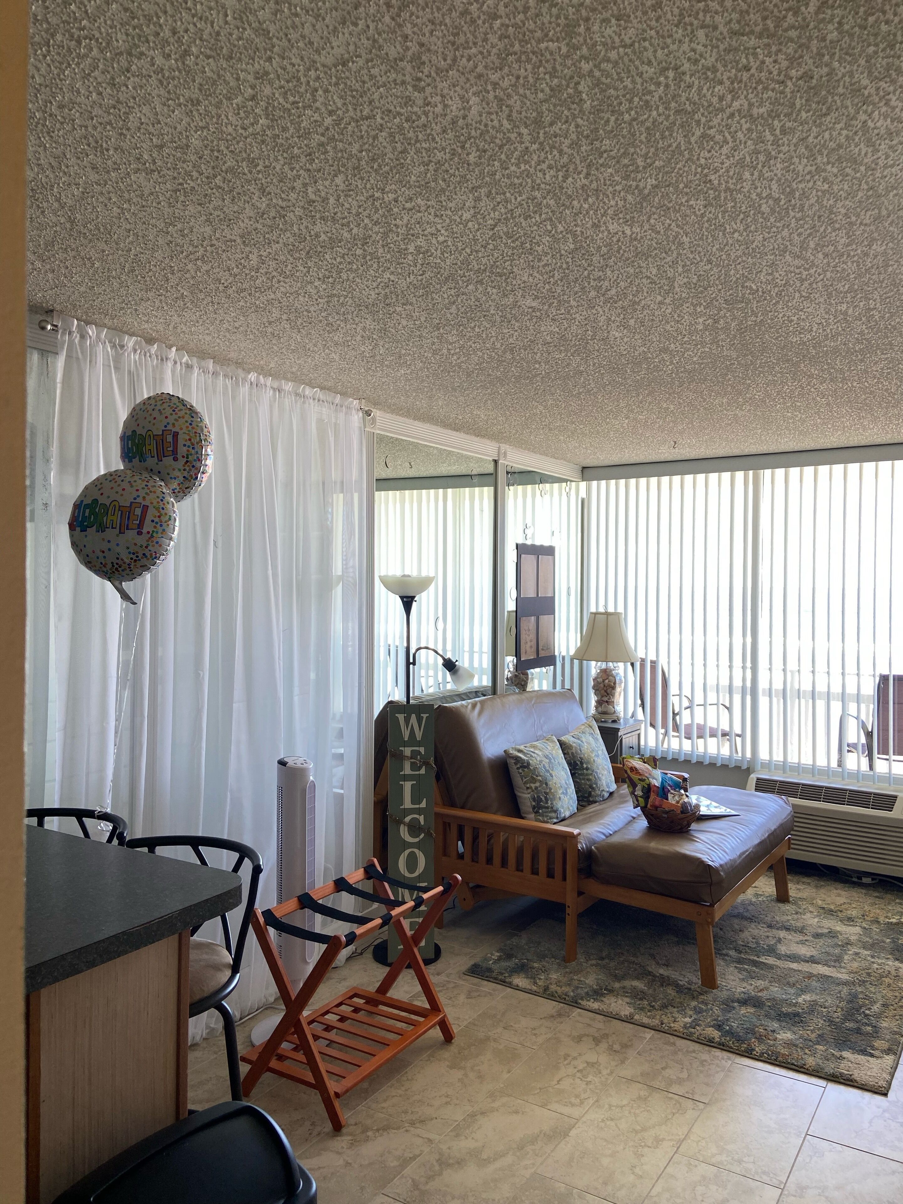 A living room with a sofa, a small table, and a chair. There are balloons with the word "Celebrate!" on them.