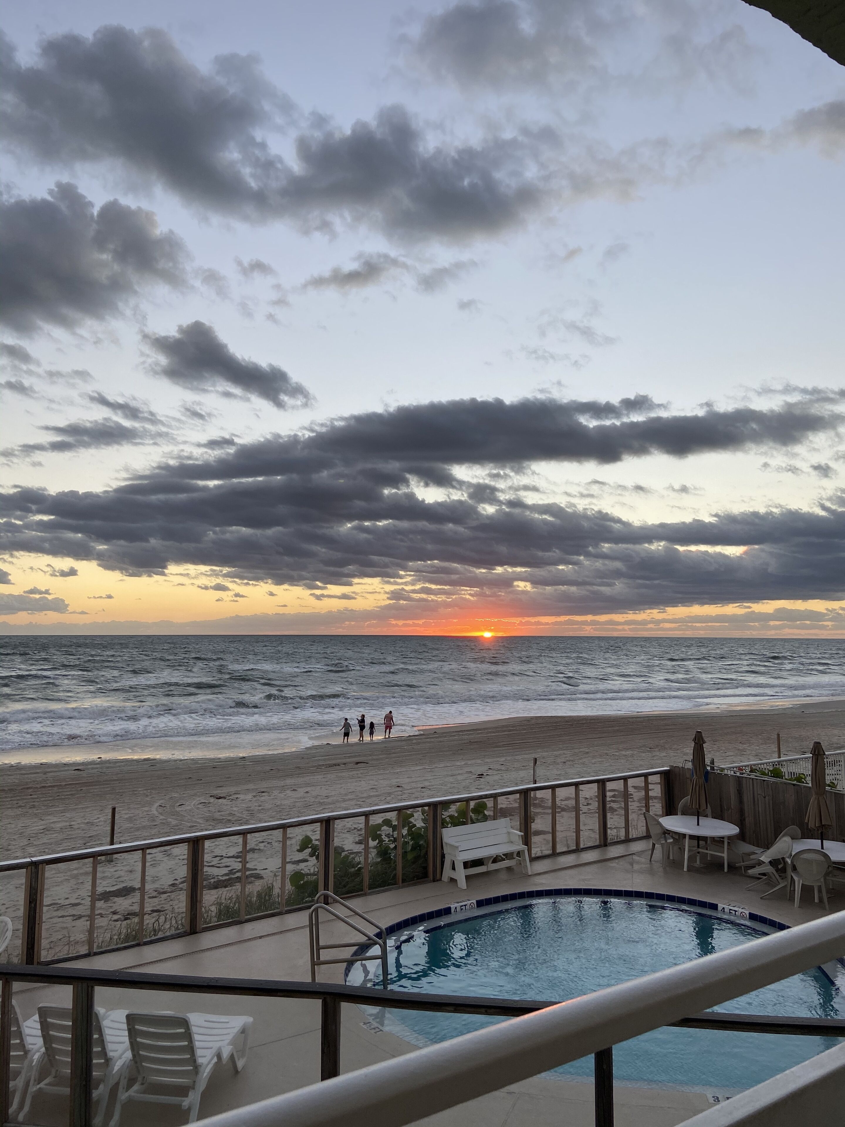 Ein Poolbereich mit Blick auf Strand und Meer bei Sonnenuntergang.